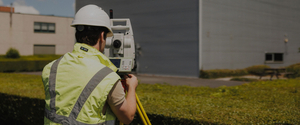 Landmeter van Sabbe met helm en fluohesje bedient een totaalstation op statief