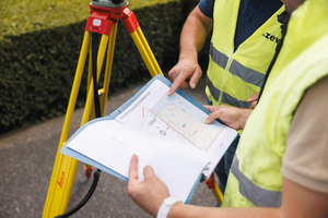 Landmeters wijzen details aan op een opmetingsplan naast een statief