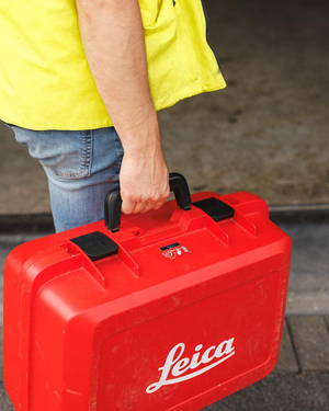 Landmeter in fluohesje draagt een rode Leica koffer met meettoestel